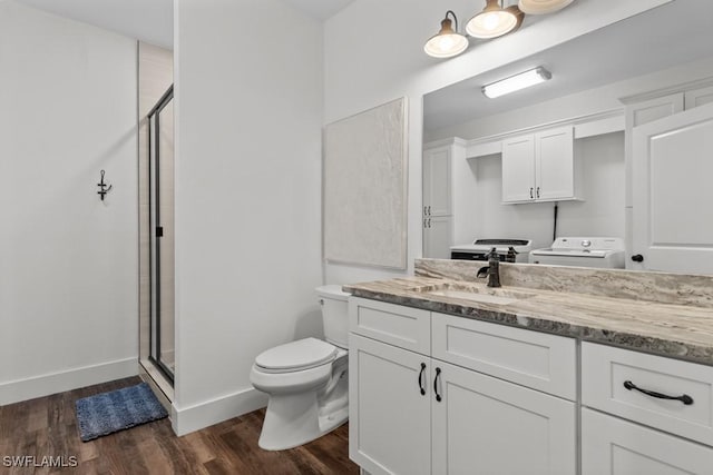 bathroom with hardwood / wood-style floors, vanity, washer / dryer, a shower with shower door, and toilet