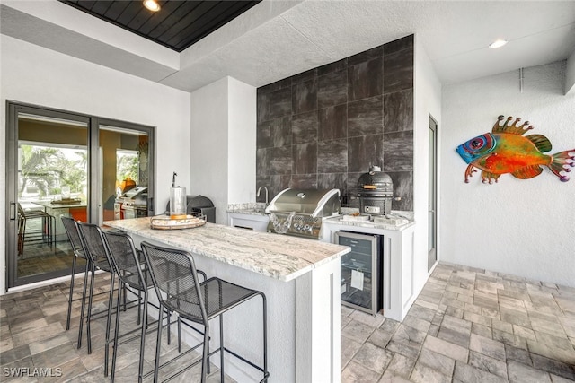 kitchen with wine cooler, a breakfast bar, white cabinetry, light stone counters, and kitchen peninsula