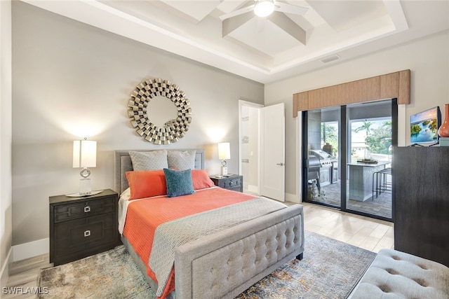 bedroom featuring ceiling fan, access to outside, light wood-type flooring, and a tray ceiling