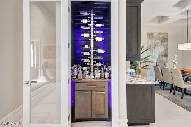 bar with stone counters, pendant lighting, dark brown cabinets, and light tile patterned floors