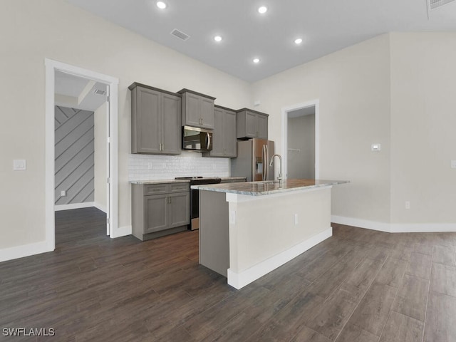 kitchen with dark wood-type flooring, gray cabinetry, a kitchen island with sink, and stainless steel appliances