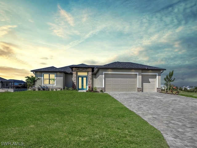 prairie-style home with stucco siding, a garage, stone siding, decorative driveway, and a lawn