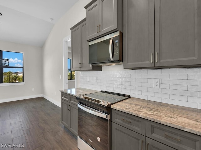 kitchen featuring decorative backsplash, lofted ceiling, light stone countertops, stainless steel appliances, and gray cabinetry