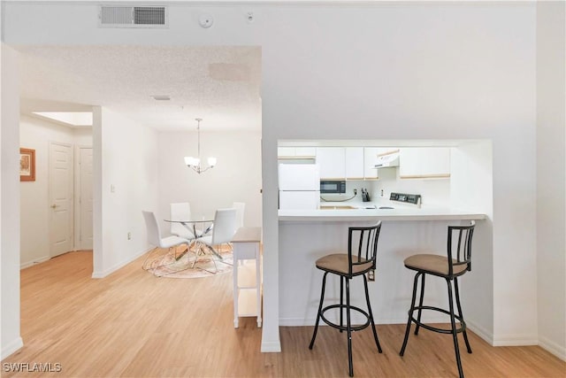 kitchen with a kitchen bar, white cabinetry, black microwave, white refrigerator, and kitchen peninsula