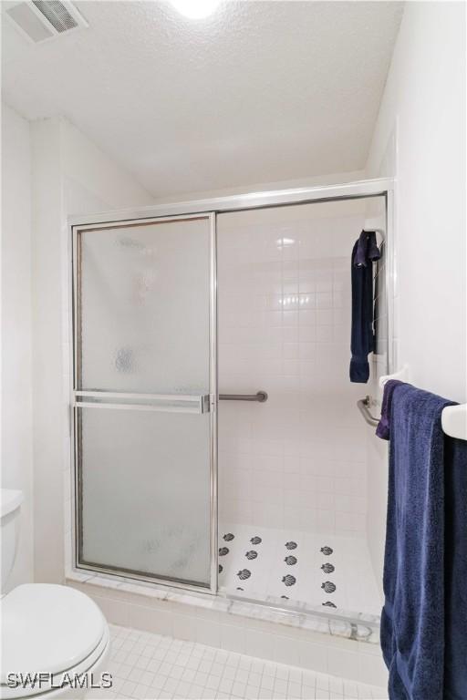 bathroom featuring tile patterned flooring, a shower with shower door, and toilet