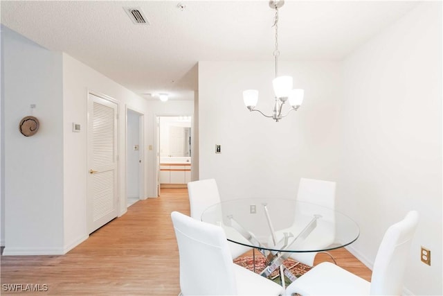 dining space with a textured ceiling, a chandelier, and light wood-type flooring