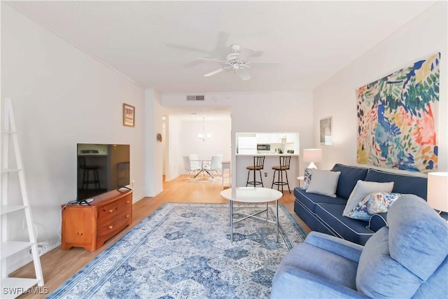 living room featuring ceiling fan with notable chandelier and light hardwood / wood-style flooring