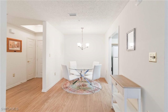 dining room with a notable chandelier, a textured ceiling, and light wood-type flooring