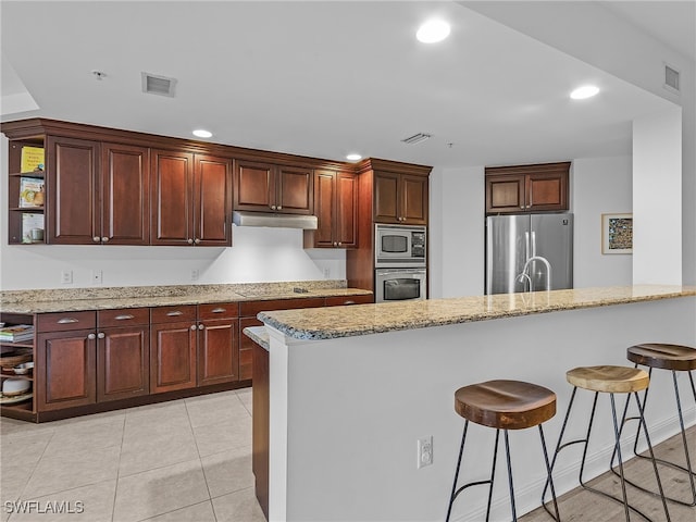 kitchen featuring light stone counters, stainless steel appliances, a kitchen breakfast bar, and light tile patterned floors