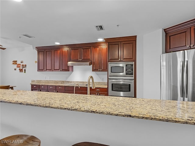 kitchen featuring light stone countertops, sink, stainless steel appliances, and a kitchen breakfast bar