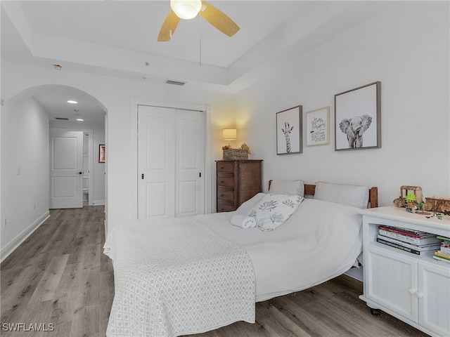 bedroom with ceiling fan, a tray ceiling, a closet, and light wood-type flooring