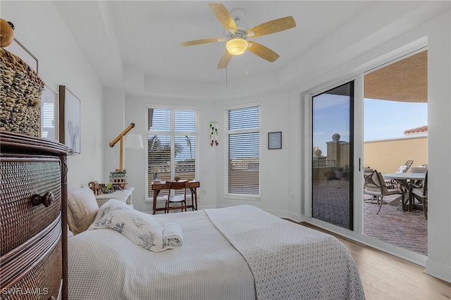 bedroom featuring access to exterior, a raised ceiling, ceiling fan, and light wood-type flooring