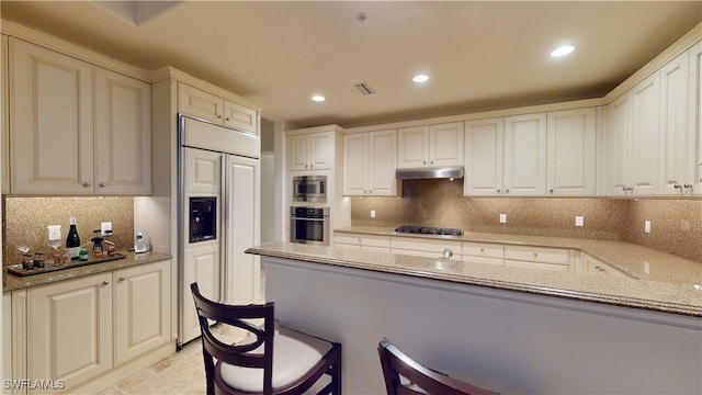 kitchen featuring tasteful backsplash, white cabinetry, built in appliances, and light stone counters