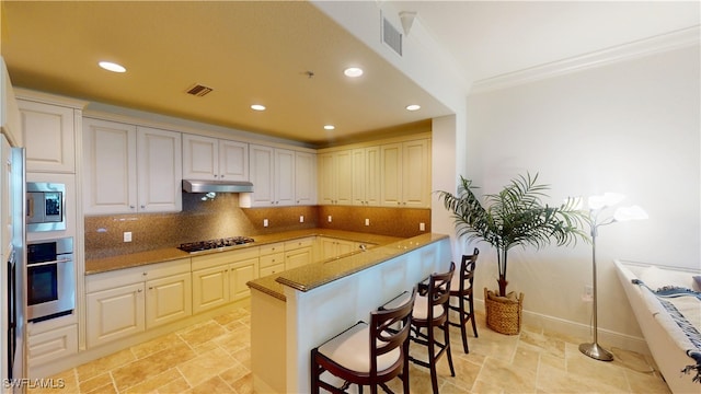 kitchen with appliances with stainless steel finishes, a kitchen breakfast bar, tasteful backsplash, stone countertops, and kitchen peninsula