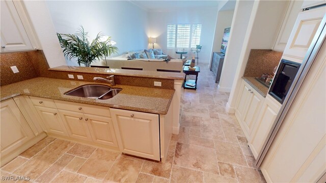 kitchen with stone finish floor, a sink, a peninsula, white cabinets, and decorative backsplash