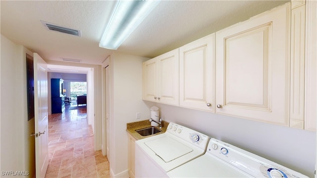 laundry room featuring washing machine and clothes dryer, visible vents, cabinet space, a textured ceiling, and a sink