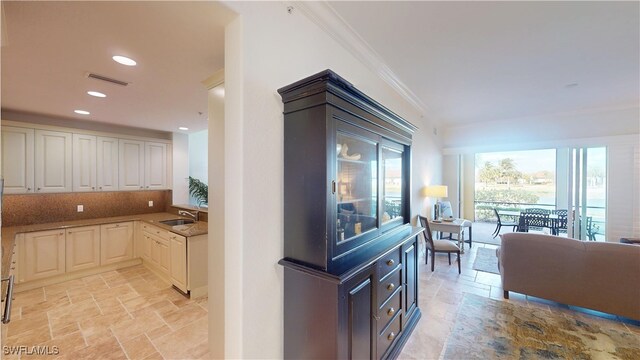 interior space featuring crown molding, stone tile floors, visible vents, and a sink