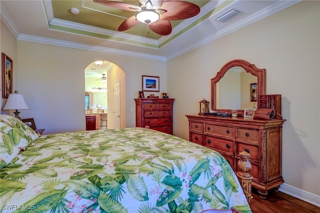 bedroom featuring dark hardwood / wood-style floors, ceiling fan, a raised ceiling, crown molding, and ensuite bath