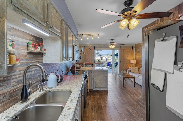 kitchen with tasteful backsplash, sink, dark hardwood / wood-style flooring, a barn door, and light stone countertops