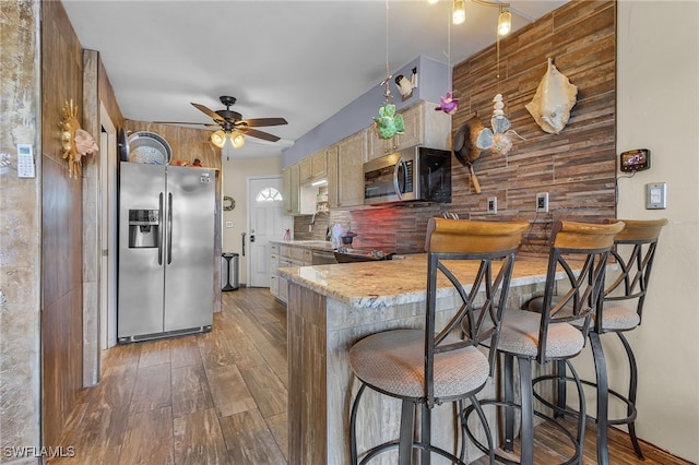 kitchen with a breakfast bar, dark hardwood / wood-style flooring, ceiling fan, stainless steel appliances, and backsplash