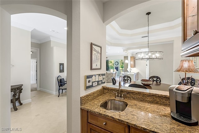 kitchen featuring stone countertops, decorative light fixtures, sink, a raised ceiling, and crown molding