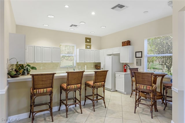 kitchen featuring white cabinets, a kitchen bar, white refrigerator with ice dispenser, light tile patterned floors, and kitchen peninsula