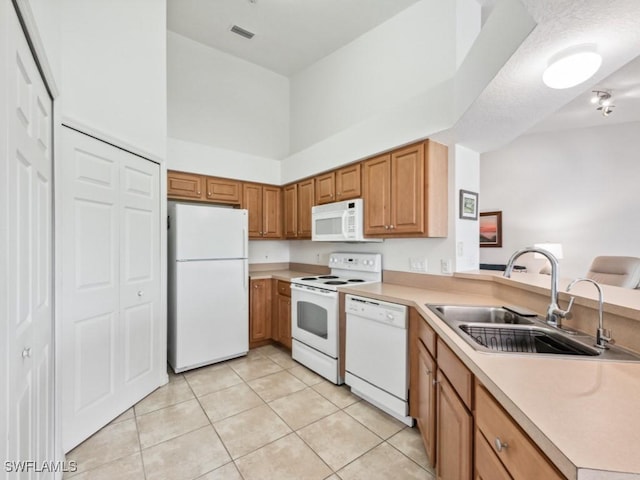 kitchen with sink, white appliances, light tile patterned floors, a towering ceiling, and kitchen peninsula