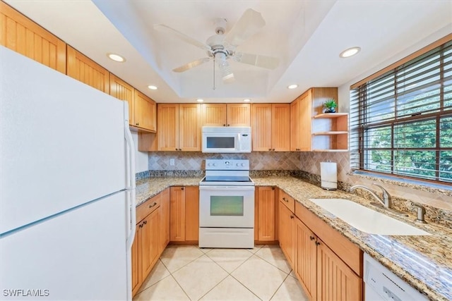 kitchen with a tray ceiling, sink, white appliances, and light stone countertops