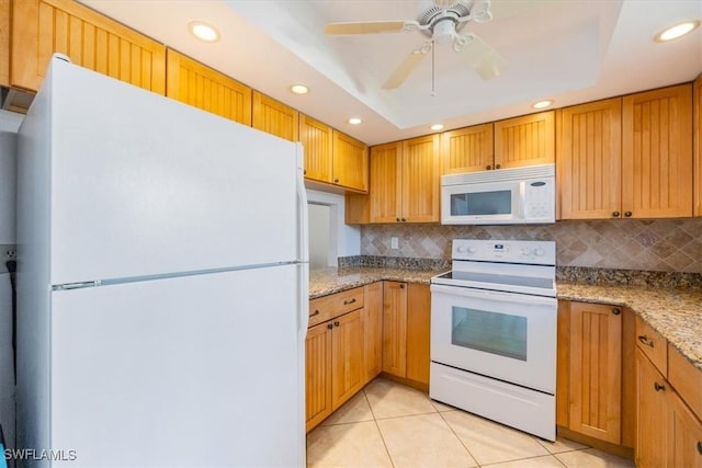 kitchen with white appliances, a tray ceiling, light tile patterned flooring, and light stone countertops