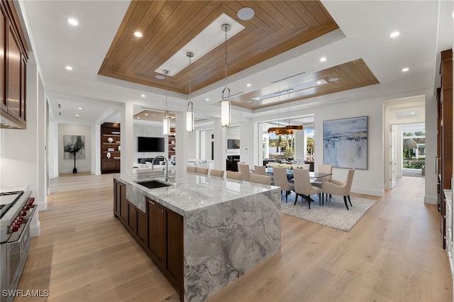 kitchen with decorative light fixtures, sink, a large island, light stone counters, and a tray ceiling