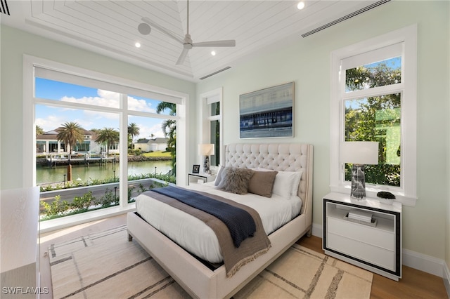 bedroom with light wood-type flooring, wooden ceiling, ceiling fan, and a water view
