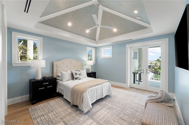 bedroom featuring french doors, access to exterior, a raised ceiling, and light wood-type flooring