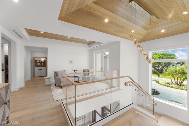 corridor with stacked washer and dryer, wooden ceiling, light hardwood / wood-style floors, and a tray ceiling