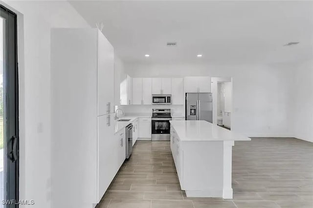 kitchen featuring stainless steel appliances, a center island, a wealth of natural light, and white cabinets