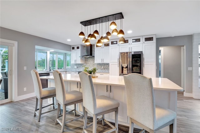 kitchen featuring tasteful backsplash, hanging light fixtures, a large island, stainless steel fridge with ice dispenser, and wall chimney range hood