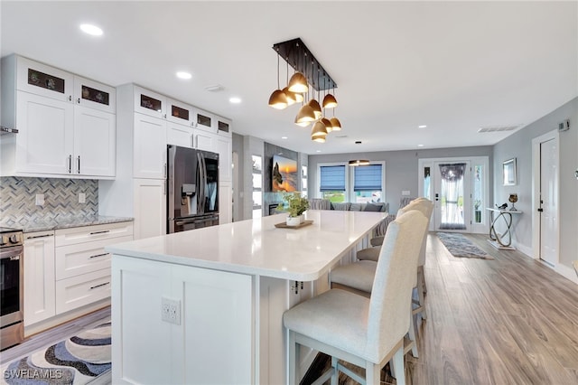 kitchen featuring stainless steel appliances, white cabinetry, hanging light fixtures, and a breakfast bar