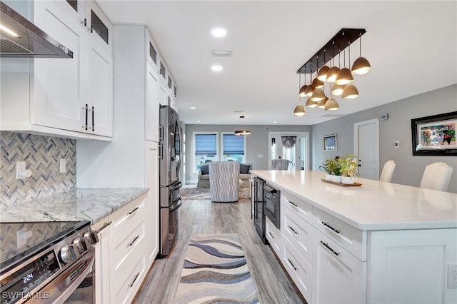 kitchen with a kitchen island, a breakfast bar, pendant lighting, white cabinetry, and wall chimney exhaust hood