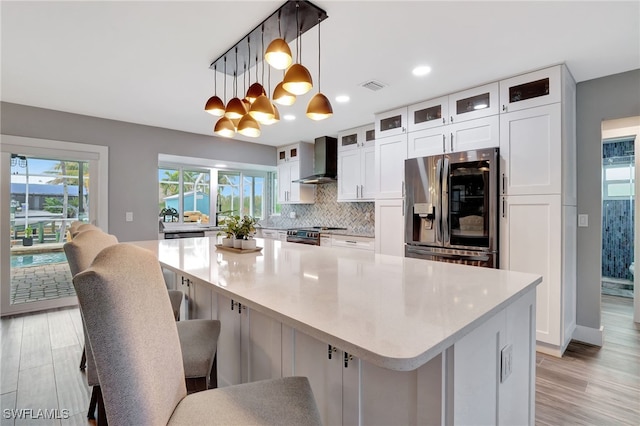 kitchen featuring wall chimney exhaust hood, white cabinetry, appliances with stainless steel finishes, and a large island