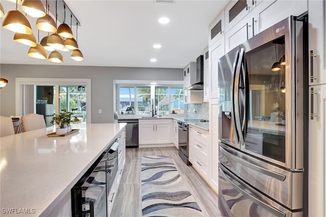 kitchen with white cabinetry, hanging light fixtures, stainless steel appliances, tasteful backsplash, and wall chimney exhaust hood