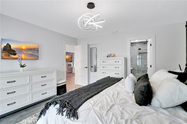 bedroom featuring an inviting chandelier, wood-type flooring, and connected bathroom