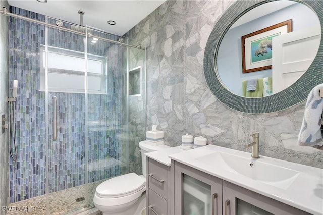 bathroom with a shower with door, vanity, tile walls, and toilet