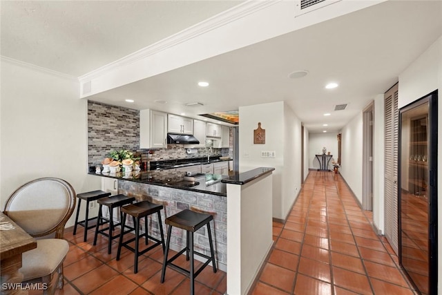 kitchen featuring white cabinetry, a kitchen bar, kitchen peninsula, and decorative backsplash