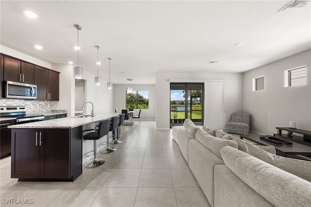 kitchen featuring a breakfast bar, a kitchen island with sink, stainless steel appliances, dark brown cabinetry, and decorative light fixtures