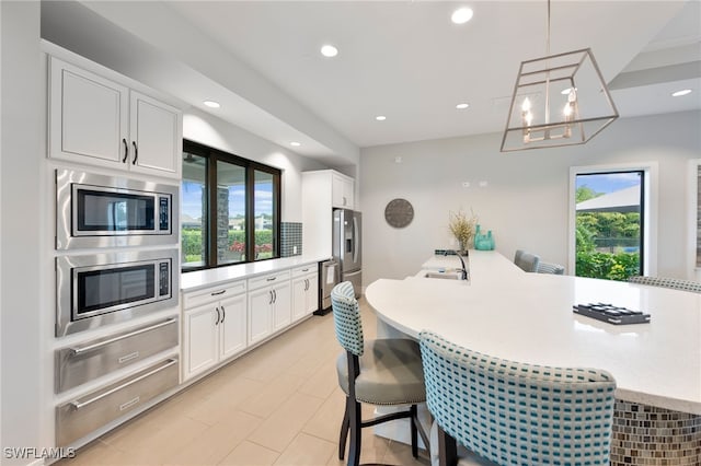 kitchen featuring white cabinetry, decorative light fixtures, stainless steel appliances, and a kitchen bar