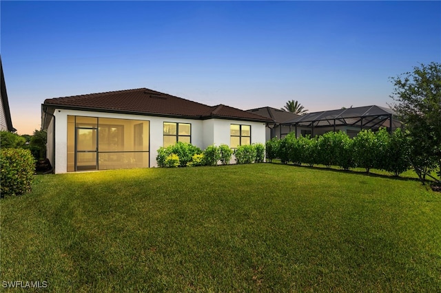 back house at dusk featuring a lawn and glass enclosure