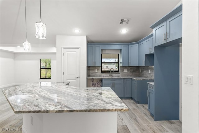 kitchen with sink, a center island, hanging light fixtures, light stone countertops, and backsplash