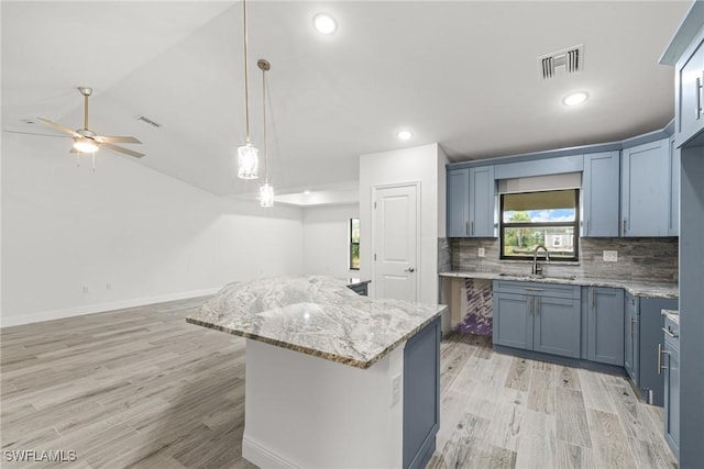 kitchen featuring sink, light stone counters, decorative light fixtures, a center island, and backsplash