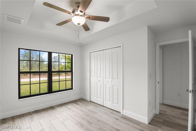 unfurnished bedroom with a closet, light hardwood / wood-style floors, a raised ceiling, and ceiling fan