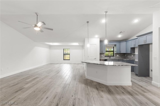 kitchen with stone countertops, a center island, vaulted ceiling, light wood-type flooring, and decorative backsplash