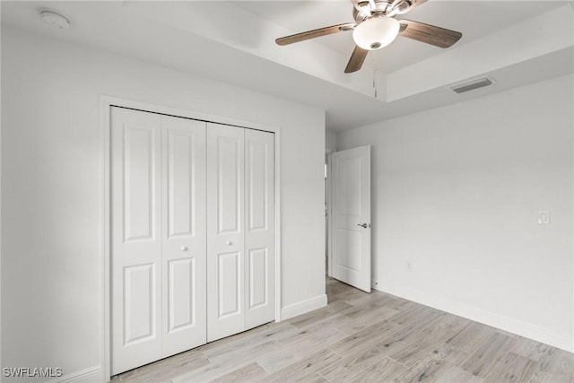 unfurnished bedroom featuring a tray ceiling, a closet, ceiling fan, and light wood-type flooring